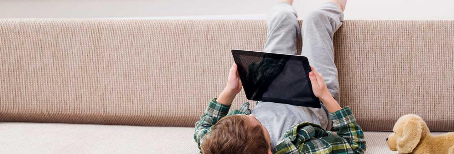 Young boy playing with an iPad on the couch of a vacation rental