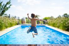 the back of a little boy jumping into a pool on a sunny day 