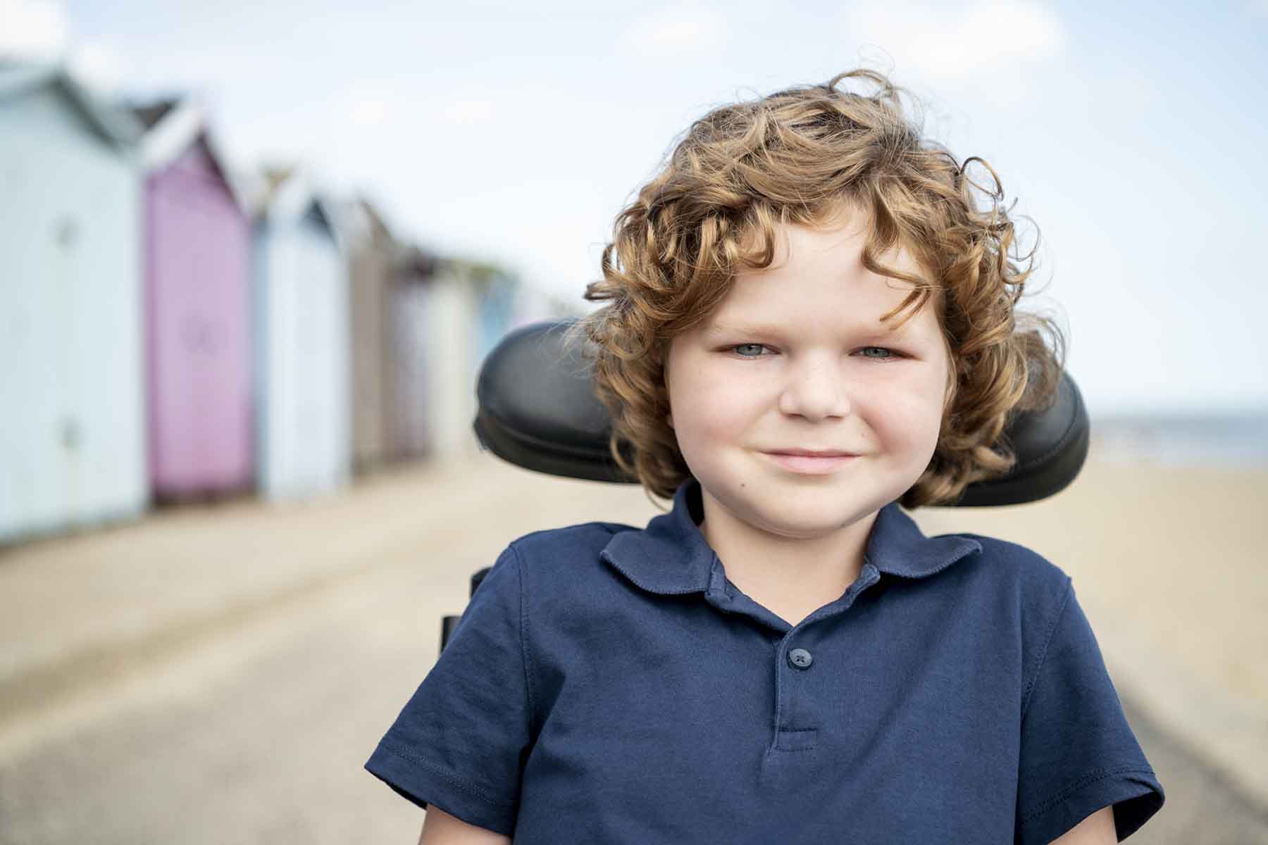 Cute young boy with wavy hair at the beach in his wheelchair