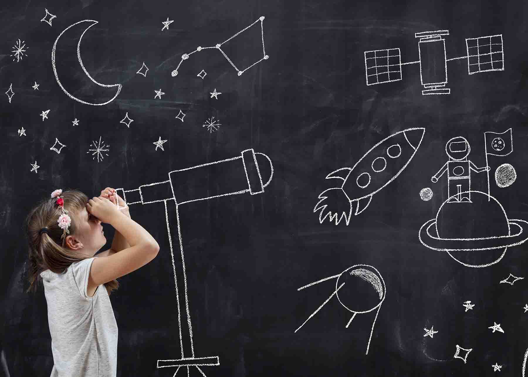 Little girl standing next to a chalk board with star exploration drawings