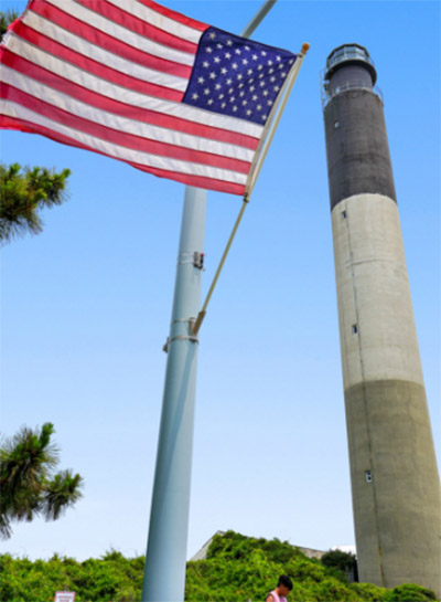 Oak Island Lighthouse on a sunny day with an American flag flying