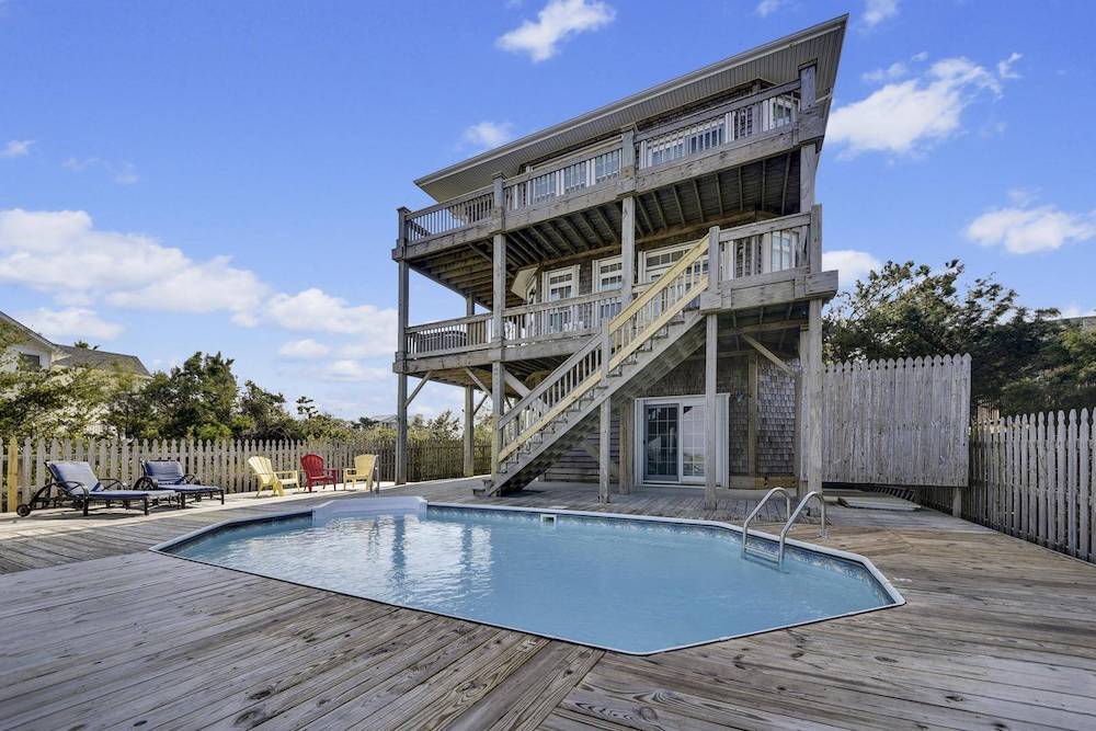 back view of very rustic weathered wood beach house featuring pool surrounded by wooden decking