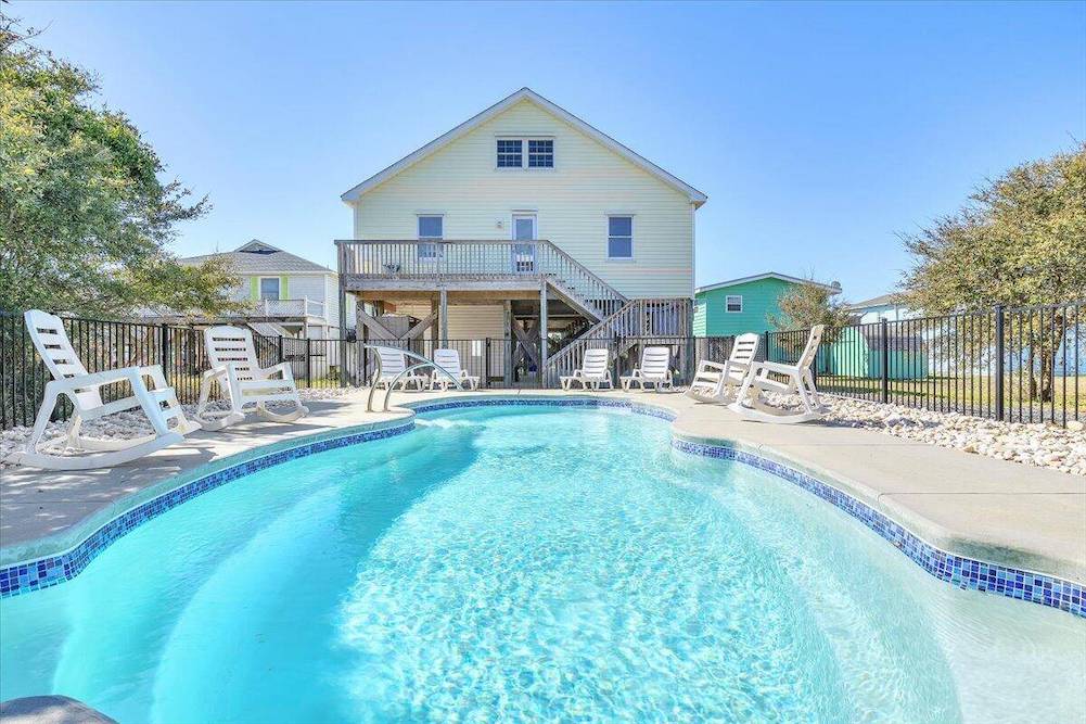 back view of cute little yellow beach house featuring in-ground pool 